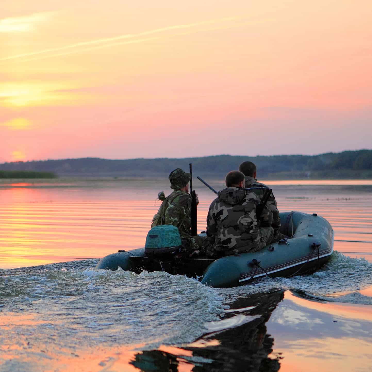 Duck hunters in inflatable boat with the sunset in front of them